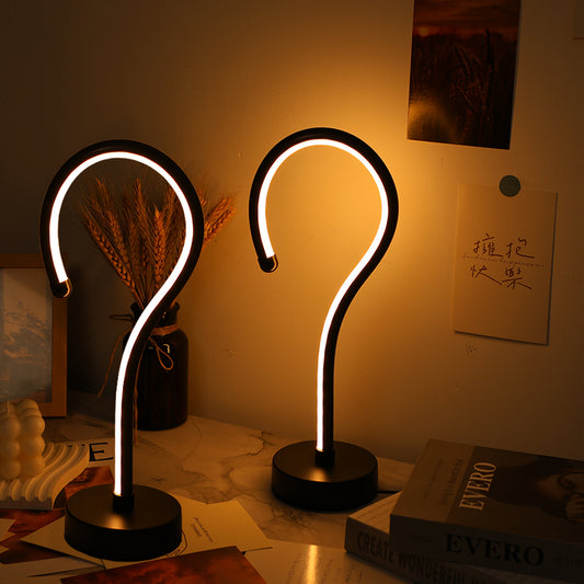 Two question mark-shaped table lamps on a desk with a warm glow.