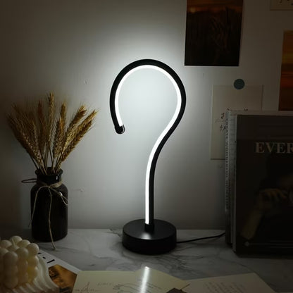 Modern table lamp with a unique design on a desk next to a vase and books.