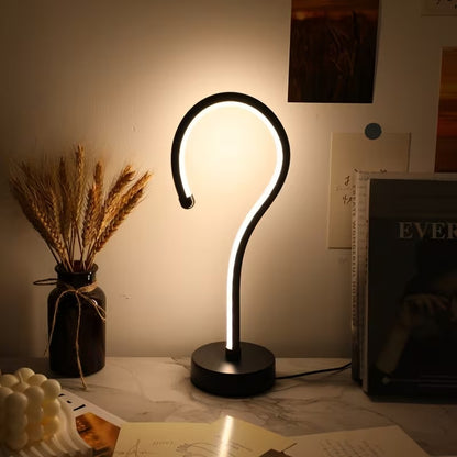 Modern table lamp with curved design on a desk next to a vase of wheat and books.