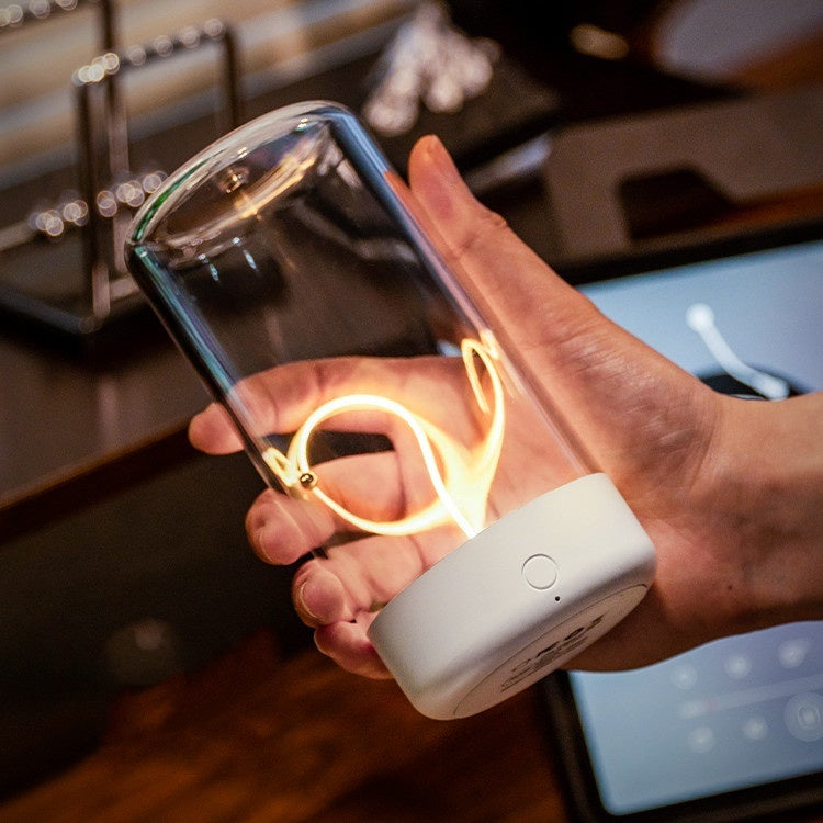 Hand holding a transparent container with glowing lights, connected to a white device, in an indoor setting.