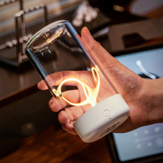 Hand holding a transparent container with glowing lights, connected to a white device, in an indoor setting.